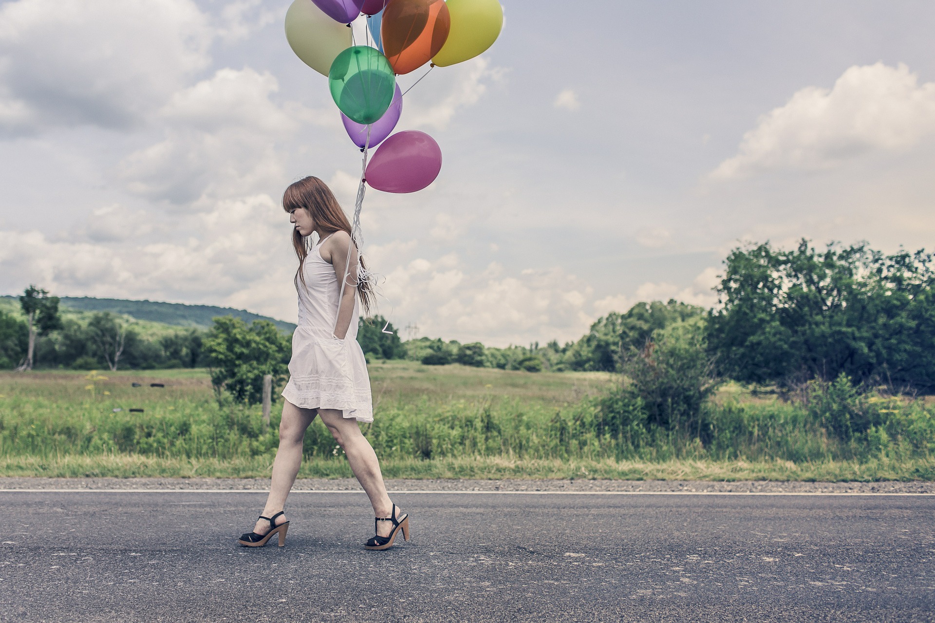 Frau im weißen Kleid auf einer Straße mit bunten Luftballons in der Hand