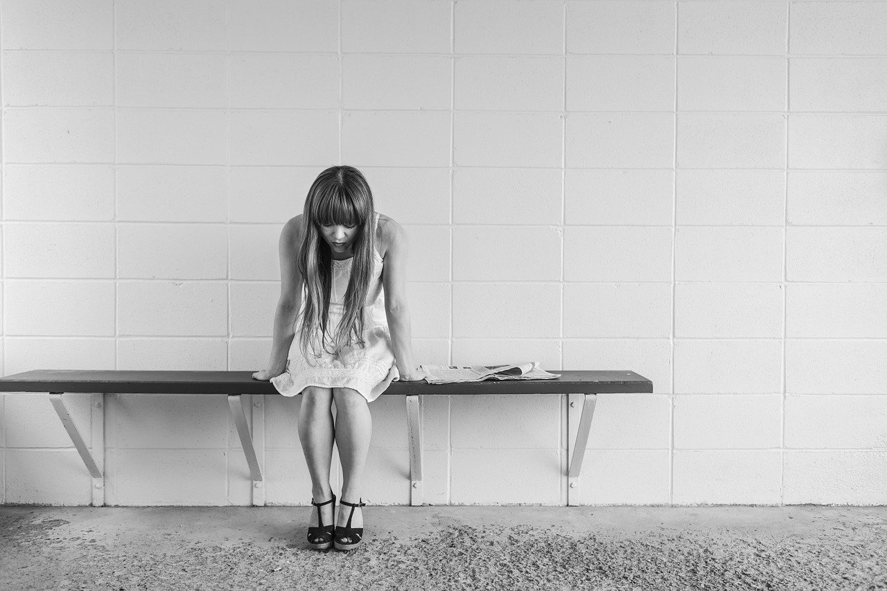 Eine Frau sitzt vornübergebeugt auf einer Bank in einem Raum, der aussieht wie Psychiatrie oder Krankenhaus