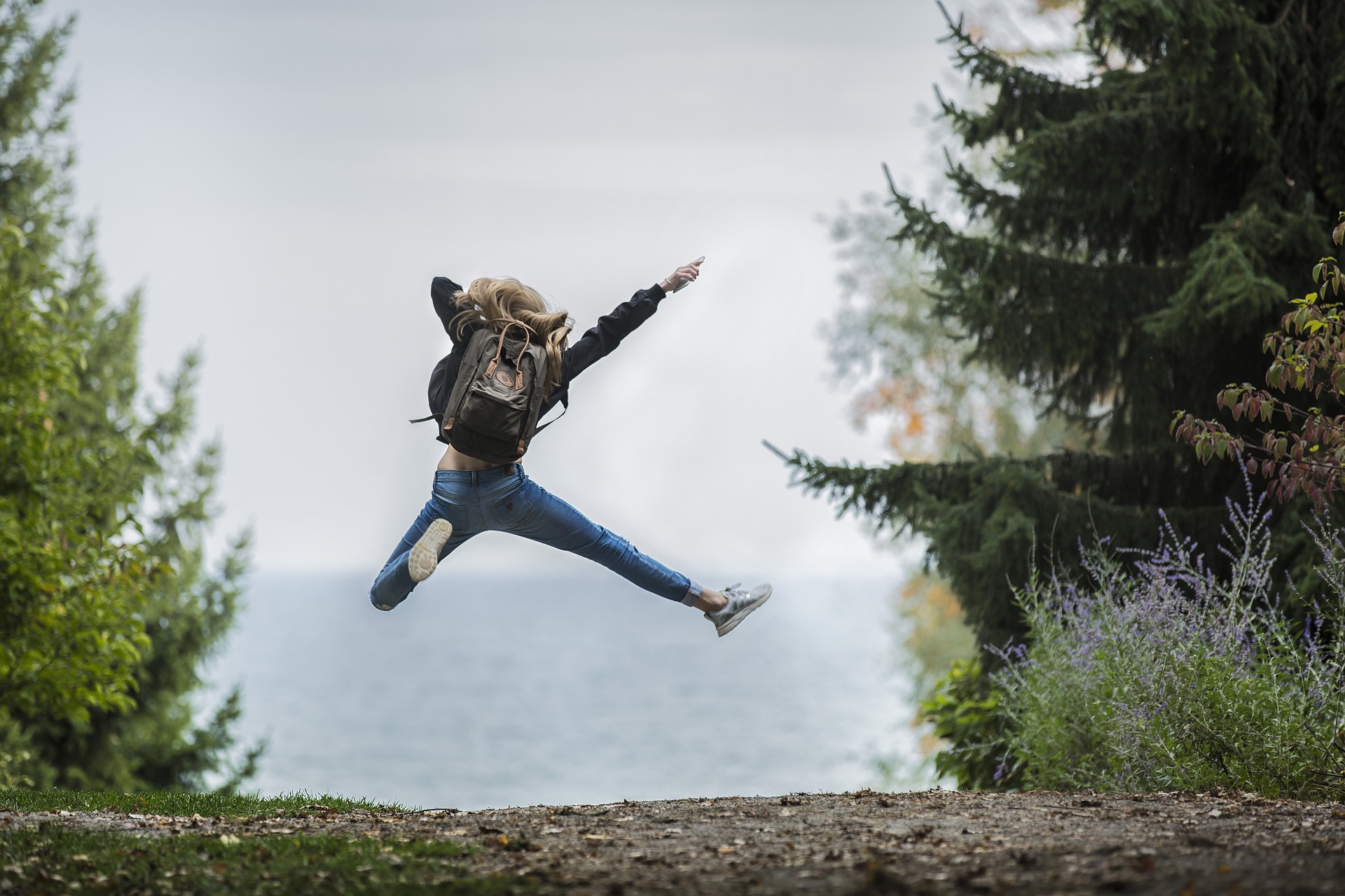 Frau mit Rucksack hüpft kraftvoll und selbstbewusst in die Luft als Sinnbild für Fülle und Glück im neuen Jahr