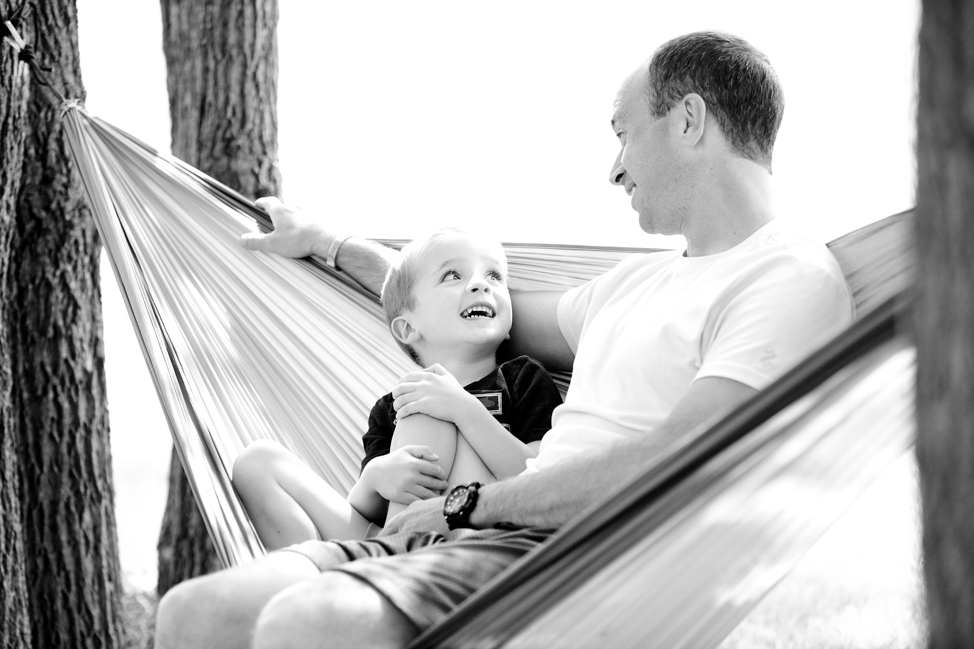 Vater und Sohn sitzen zusammen in der Hängematte und lächeln sich liebevoll an
