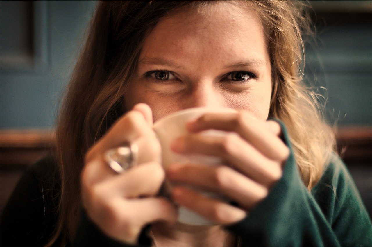 Frau mit Kaffeetasse, die ihr halbes Gesicht verdeckt, die Augen scheinen zu lachen