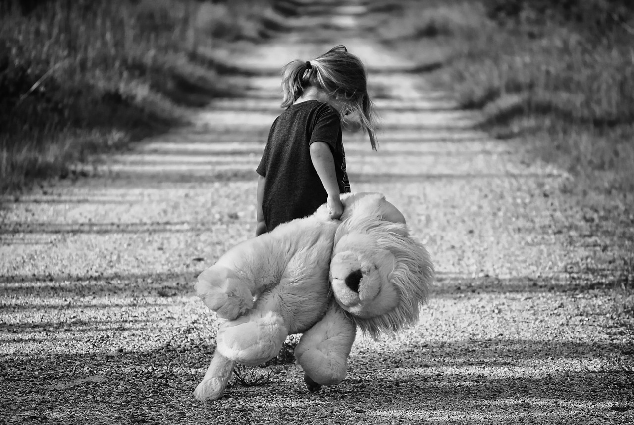 Kleines Mädchen auf einem sandigen Weg hat einen großen Kuscheltier-Löwen in der Hand