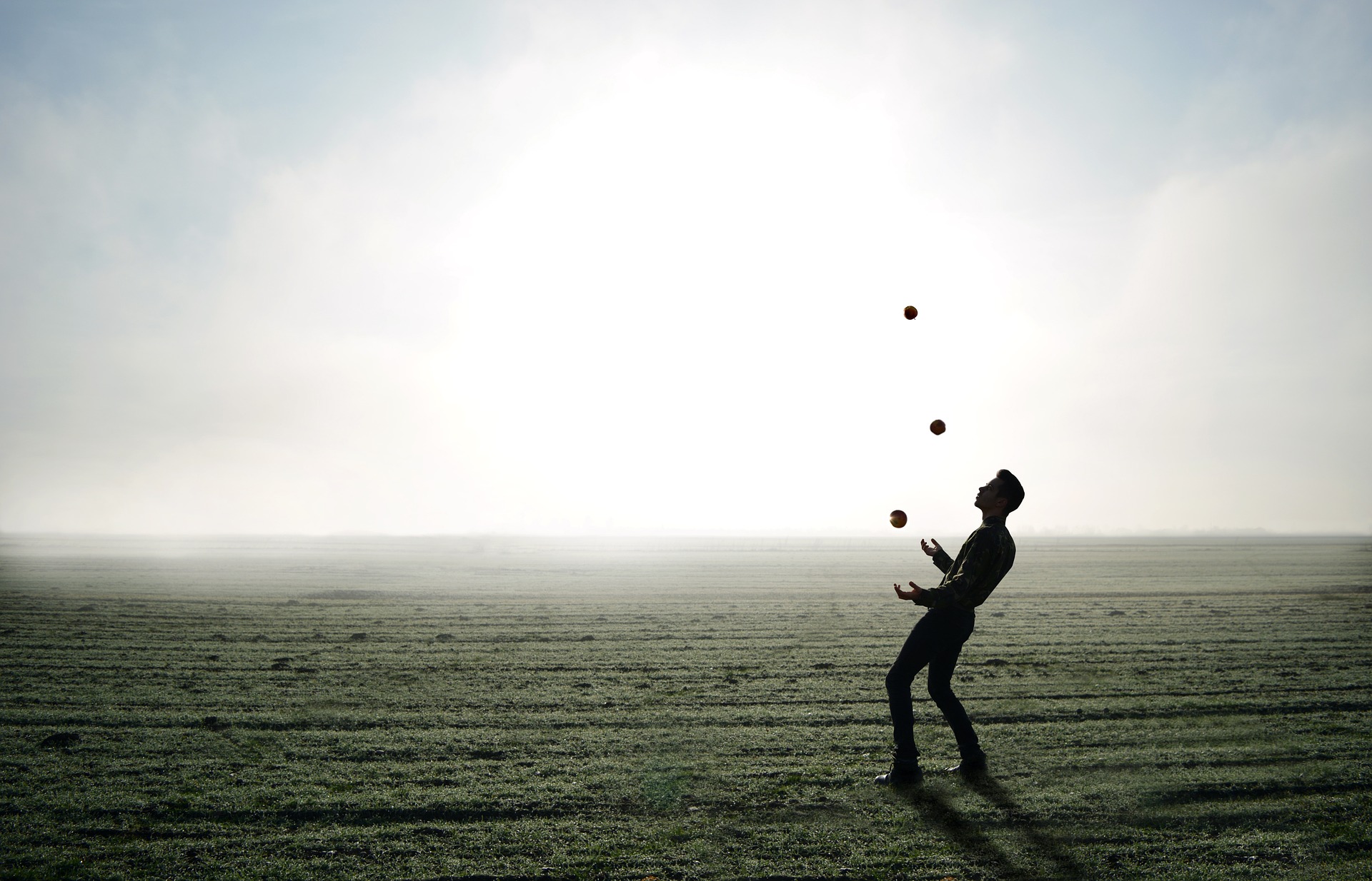 Ein Mann jongliert im Gegenlicht mit drei Bällen auf einem Feld, als Sinnbild für das Auflösen von negativen Gefühlen in drei Schritten.