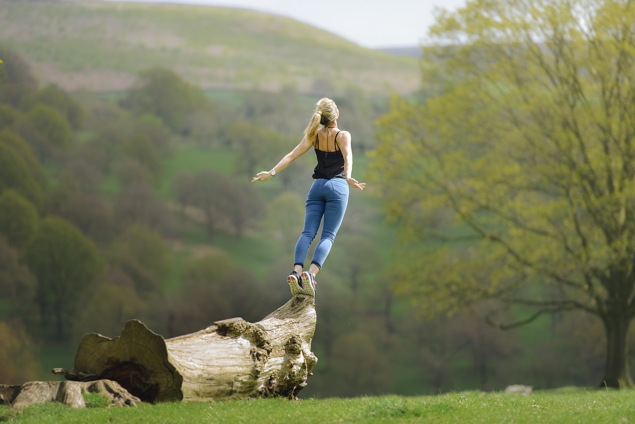 Frau auf einem Holzstamm zum Sprung bereit als Sinnbild, dass sie ihre negativen Gefühle loslassen will