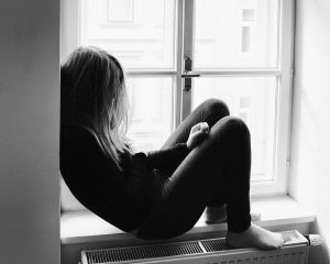 Frau sitzt zusammengesunken im Fenster als Sinnbild für den Schmerz von Trauma