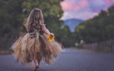 Kleines Mädchen von hinten zu sehen mit einer Blume in der Hand als Sinnbild für Selbstvertrauen