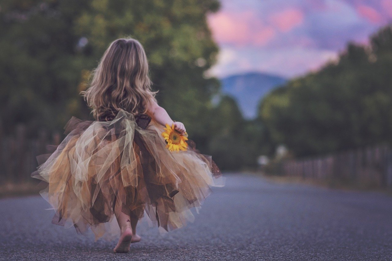 Kleines Mädchen von hinten zu sehen mit einer Blume in der Hand als Sinnbild für Selbstvertrauen