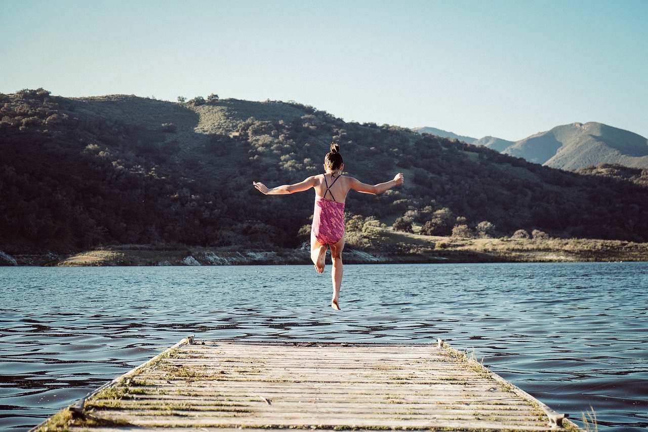 Mädchen auf einem Steg springt ins Wasser als Sinnbild für den Mut seine Träume zu leben