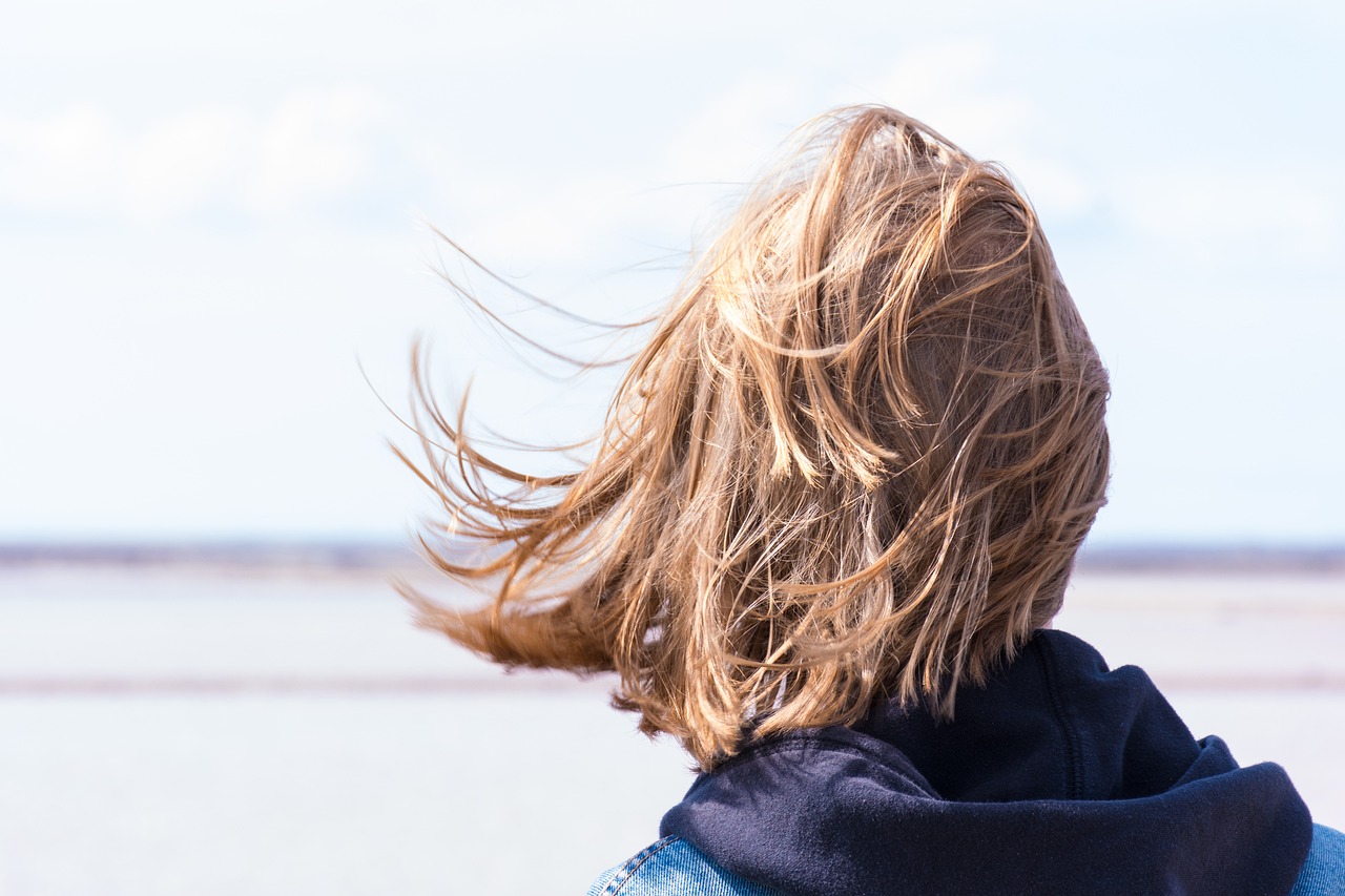 Frau im Wind blickt mutig auf Meer als Sinnbild für den Mut zur Veränderung