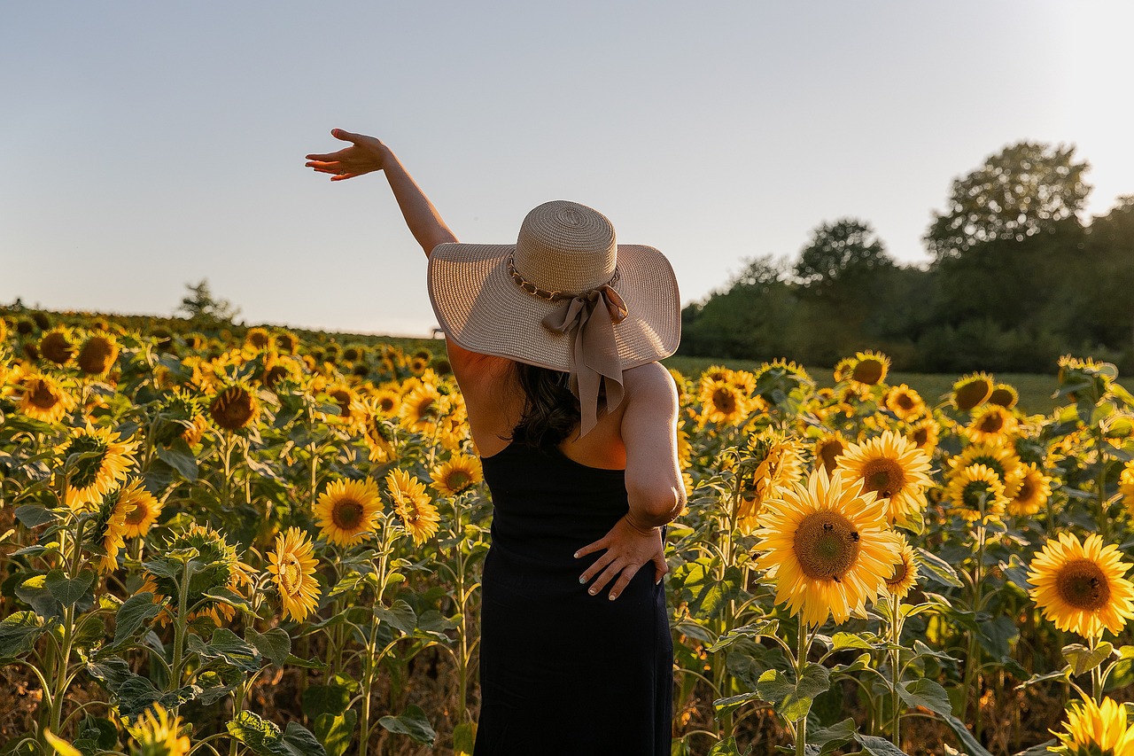 Frau mit einem Hut vor einem Feld mit Sonnenblumen als Sinnbild für Lebensfreude